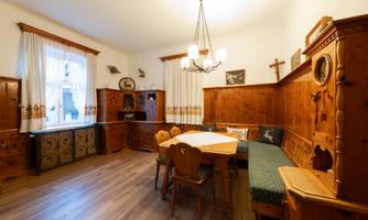 A cozy dining area with wooden furniture and a large table. Large windows let in plenty of light and give the space an inviting atmosphere.