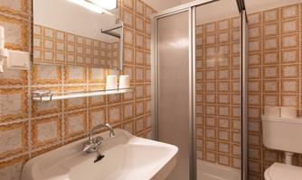 A modern bathroom with a shower cabin and a white sink. The walls are decorated with a yellow tile pattern.