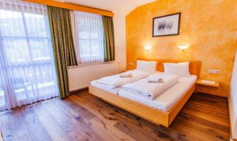 A cozy bedroom with a double bed and wooden floor. Large windows provide plenty of daylight and an inviting atmosphere.