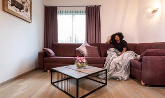A cozy living room setup with a purple sofa and a modern coffee table. A person is sitting relaxed on the sofa with a blanket.