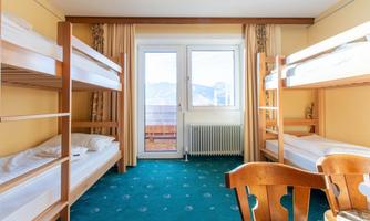 A simple room with two bunk beds and a table. Large windows provide a view outside.