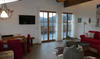 A cozy living room with red furniture and large windows. The room has a warm atmosphere and a view of the mountains.