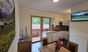A modern kitchen with a dining table and a beautiful view through large windows. On the wall hangs a picture of the mountain landscape.