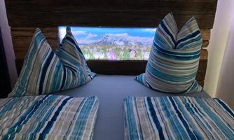 A cozy bed with striped pillows and bedding. In the background is a decorative headboard with landscape lighting.