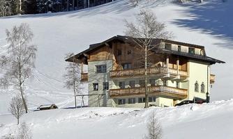 A charming house amidst a snow-covered landscape. Surrounded by trees and mountains, it conveys a serene winter atmosphere.