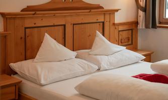 A cozy bedroom with a wooden bed and large, white pillows. The warm wood tones create an inviting atmosphere.