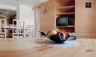 A cozy living space with wooden shelves and a dining table. On the table sits a bowl of apples.