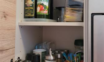 A kitchen cupboard that contains various bottles and containers. Among them are oil, vinegar, and spices.