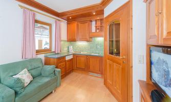 A cozy kitchen with wooden cabinets and a green sofa. The room has large windows and warm light.