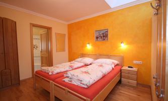A cozy bedroom with two beds covered in floral bedding. The walls are painted in a warm yellow tone and there is light wooden flooring.