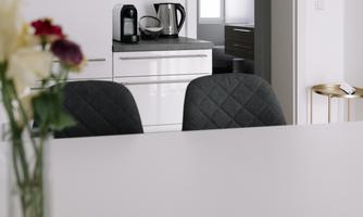 A modern kitchen with elegant furniture and a table. In the background, another room is visible.