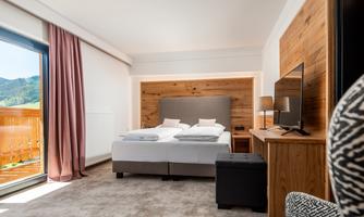 A modern bedroom with two beds and wood paneling. The room has large windows and a cozy atmosphere.