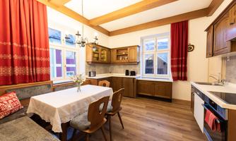A cozy kitchen with wooden furniture and a dining group. Red curtains and a bright ambiance create an inviting atmosphere.