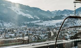 A picturesque winter landscape with snow-covered mountains and a small village in the valley. The gentle sun shines over the snowy scene.