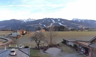 A picturesque landscape with snow-capped mountains in the background. In the foreground, there is a field and some houses.