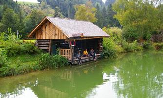 A picturesque wooden house by the shore of a green pond. People sit relaxed on the veranda and enjoy nature.