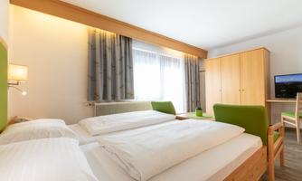 A modern bedroom with two beds and a desk. The room is bright and cheerfully furnished, with a window that lets in daylight.