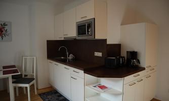 A modern kitchenette with white cabinets and a dark countertop. A small dining table with chairs is next to it.