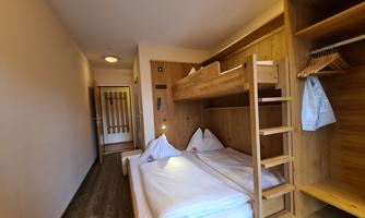 A cozy room with a double bed and a bunk bed. The walls are made of wood, and there is an open wardrobe.