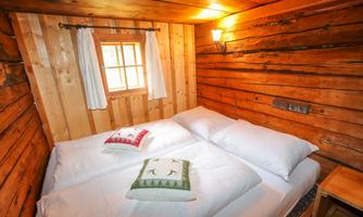 A cozy room with wooden paneling and two beds. The window lets in a lot of light and there is rustic decoration.