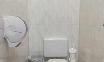 A simple bathroom with a toilet and tiled walls. A paper towel dispenser and a waste bin are also available.