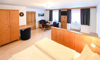 A cozy room with wooden furniture and a double bed. There is a seating area with a table and chairs as well as windows with curtains.