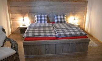 A cozy bedroom with a wooden bed and checkered blankets. Next to the bed, there are two lamps on wooden tables.