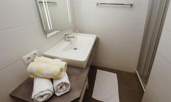 A modern bathroom with a sink, towels, and a large mirror. The walls are bright and clean, and there is a shower cubicle.