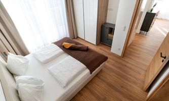 A modern bedroom with a comfortable bed and natural light. The floor is made of wood, and the decor is simple and elegant.
