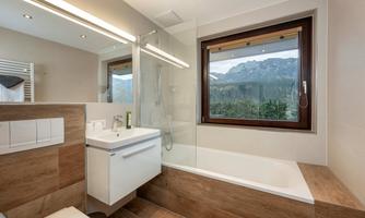 A modern bathroom with a shower and a bathtub. Through the window, you can see a beautiful mountainous landscape.