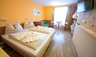 A modern room with two beds and cozy furnishings. The walls are painted in warm colors, and there is a sitting area with a table and chairs.