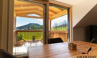A bright room with a wooden table and large windows that open onto a balcony overlooking a green landscape and hills. The decor is modern and inviting.