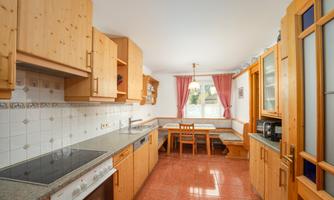 A modern kitchen with wooden furniture and bright walls. The room has a dining area with a table and chairs, as well as plenty of daylight.