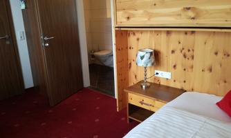A cozy room with wood paneling and a single bed. In the background, doors to a bathroom and another room are visible.
