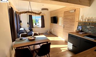 A modern living-dining room with wood decor and large windows that let in a lot of light. A dining table with chairs and a cozy seating area are visible.