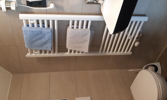 A modern bathroom with a radiator and hanging towels. Next to the sink is a toilet.