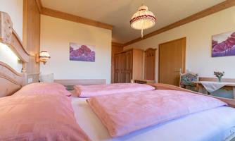 A cozy bedroom with a large bed and pink pillows. The bright decor and decorative lamps create an inviting atmosphere.