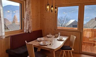 An inviting dining area with a wooden table and cozy chairs. Large windows provide a view of the mountains and let in plenty of daylight.