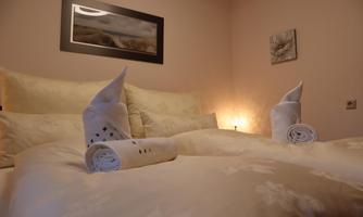 A cozy bedroom with a double bed and decorative towels. Soft light and gentle colors create an inviting atmosphere.