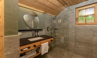 A modern bathroom with a wooden ceiling and attractive tiles. It has a shower, a sink, and a large mirror that reflects in the room.
