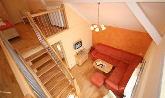 A bright and inviting living room with a red sofa and wooden floor. A staircase leads to the upper area of the room.