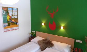 A cozy room with a large double bed and a green wall design. A painting and a stylized deer silhouette hang on the wall.