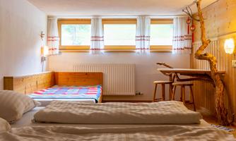 A cozy room with two beds and wooden decor. Large windows provide plenty of daylight.