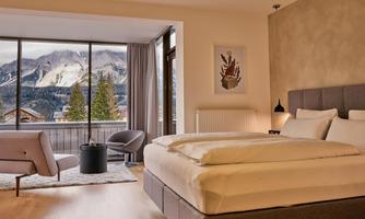 A modern bedroom with a view of the mountains. Large windows let in plenty of light and offer a beautiful view of nature.