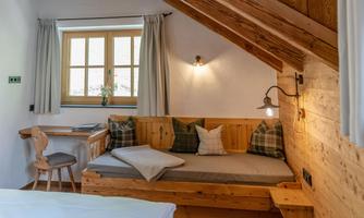 A cozy room with wooden paneling and large windows. There is a seating area with cushions and a table.