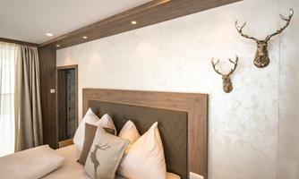 A modern bedroom with a large bed and several pillows. Two deer antlers hang on the wall, the ambiance is cozy and inviting.
