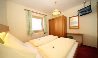 A cozy bedroom with two single beds and warm colors. There is a desk, a television, and a window with a view outside.