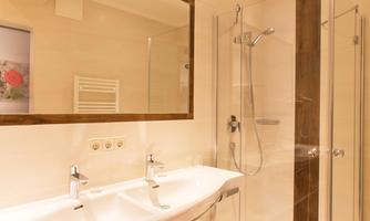A modern bathroom with a shower and two sinks. The walls are light, and there are wooden elements for a warm atmosphere.