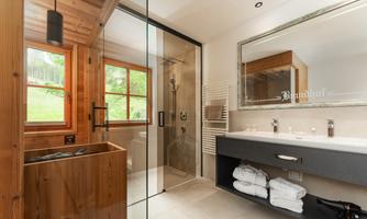 A modern bathroom with wooden details and large windows. The shower is separated by a glass wall, and fresh towels are ready.