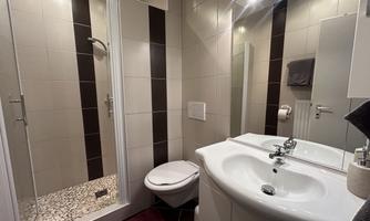 A modern bathroom with a shower and a sink. The walls are brightly tiled, and there is a wall-mounted mirror.